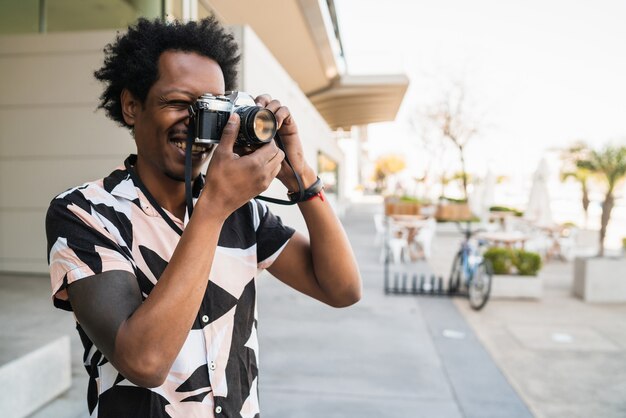 Retrato de hombre afro tomando fotografías con la cámara mientras camina al aire libre en la calle