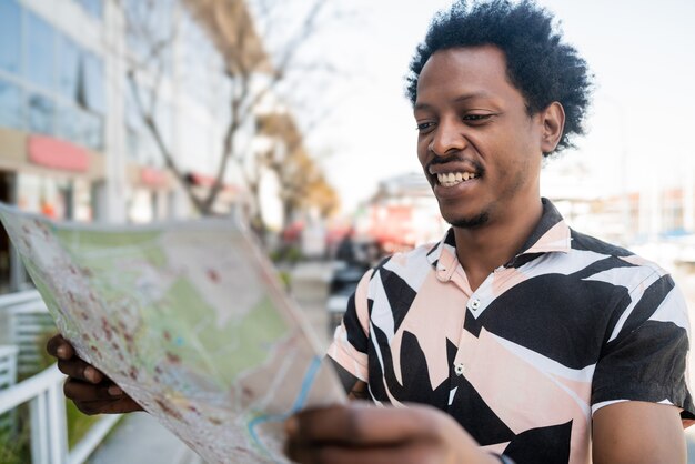 Retrato de hombre afro turista buscando direcciones en el mapa mientras camina al aire libre en la calle