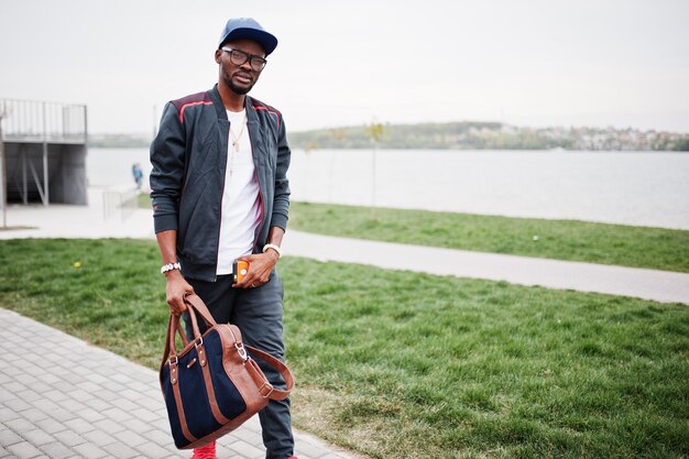 Retrato de hombre afroamericano con estilo en gorra de ropa deportiva y gafas caminando con bolso Hombres negros modelo moda callejera