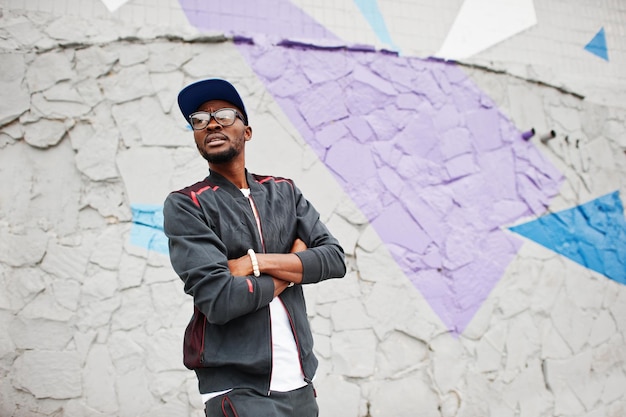 Foto gratuita retrato de hombre afroamericano con estilo en gorra de ropa deportiva y gafas contra la pared de color hombres negros modelo moda callejera