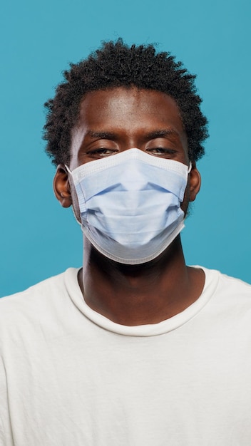 Retrato de hombre afroamericano con mascarilla para protegerse del coronavirus en estudio. Cerca de la persona negra mirando a la cámara mientras tiene una máscara protectora en la cara sobre el fondo.