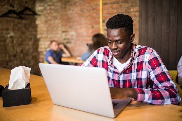 Retrato de hombre afroamericano sentado en un café y trabajando en una computadora portátil.