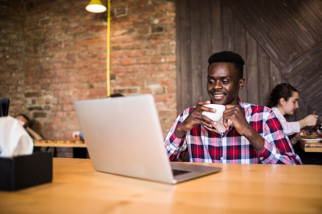 Retrato de hombre afroamericano sentado en un café y trabajando en una computadora portátil.