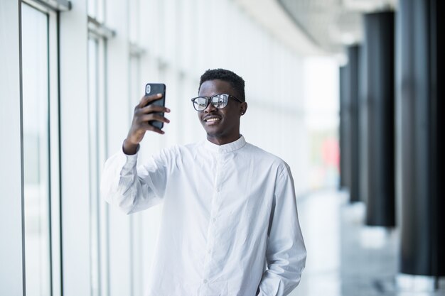 Retrato de un hombre afroamericano en smarphone en el fondo de los edificios de oficinas.