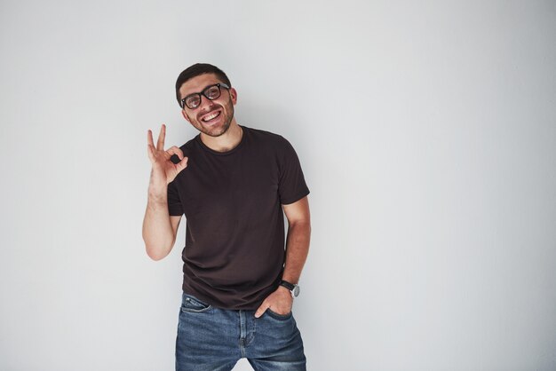 Retrato de un hombre alegre en camiseta y anteojos y mostrando signo ok