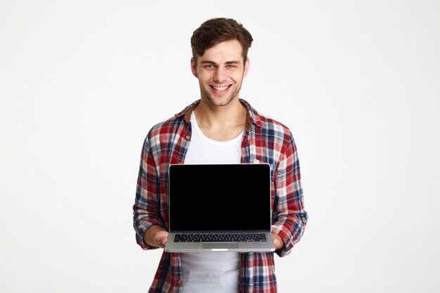 Retrato de un hombre alegre feliz mostrando portátil en pantalla en blanco