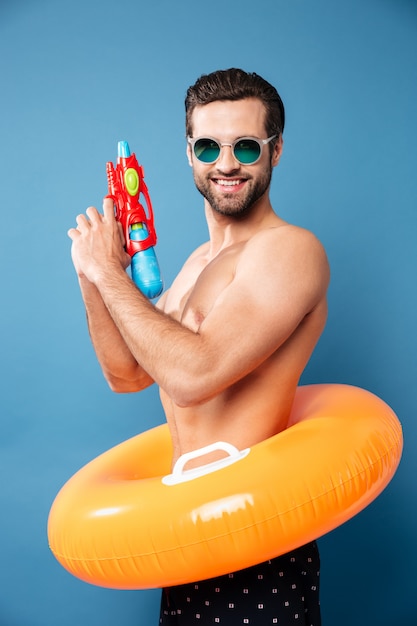 Retrato de hombre alegre mirando la cámara con pistola de agua