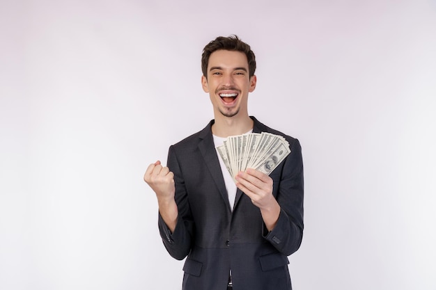 Retrato de un hombre alegre que sostiene billetes de dólar y hace gesto de ganador apretando el puño sobre fondo blanco.