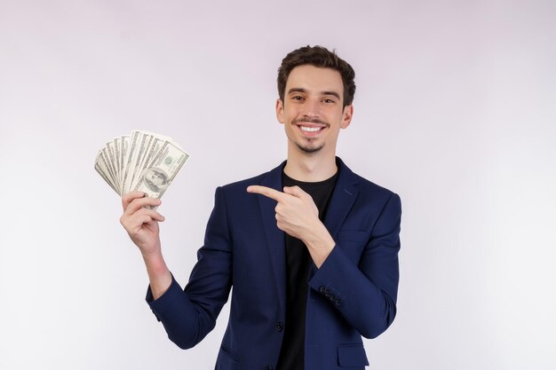 Retrato de un hombre alegre señalando con el dedo un montón de billetes de dinero sobre fondo blanco.