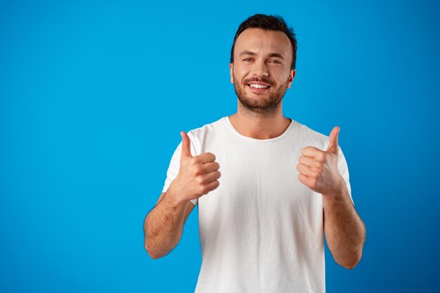 Retrato de hombre alegre sonriendo y mostrando el pulgar hacia arriba sobre fondo azul.