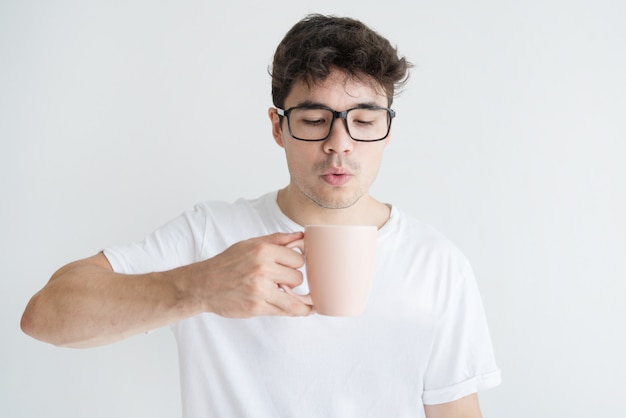 Retrato del hombre asiático joven que sopla en el café caliente en taza