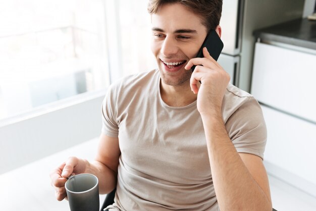 Retrato de hombre atractivo alegre hablando por teléfono en casa