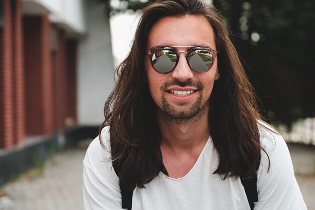 Retrato hombre atractivo con gafas de sol en escena urbana sonriendo