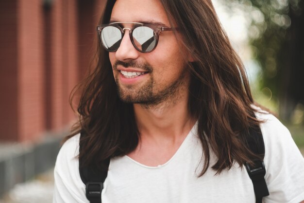 Retrato hombre atractivo con gafas de sol en escena urbana sonriendo