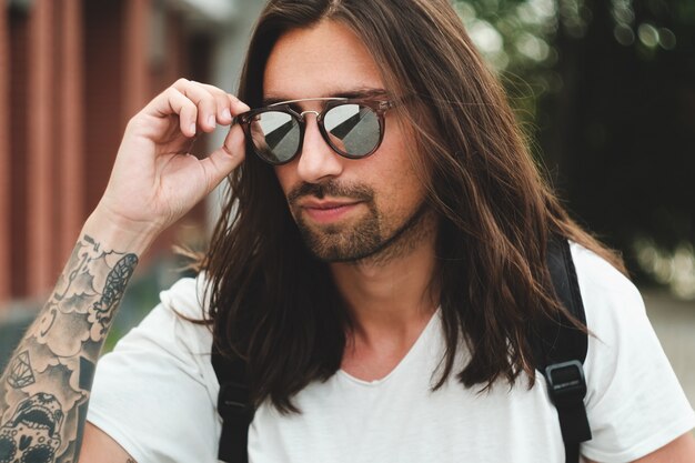 Retrato hombre atractivo con gafas de sol en escena urbana sonriendo