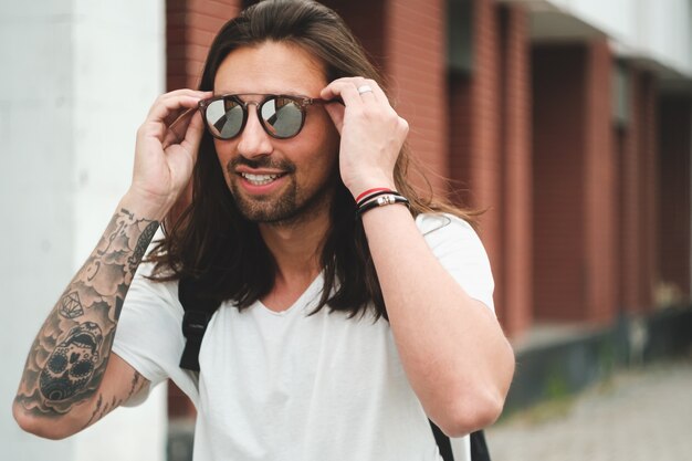 Retrato hombre atractivo con gafas de sol en escena urbana sonriendo