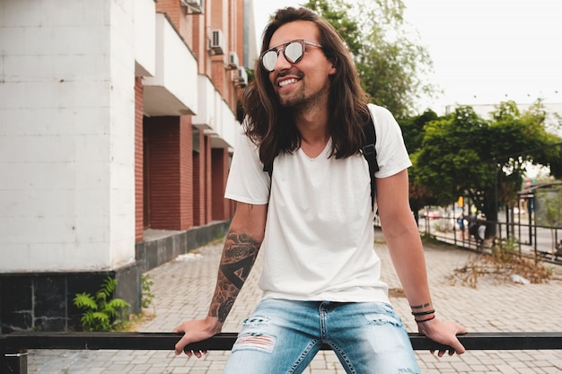 Retrato hombre atractivo con gafas de sol en escena urbana sonriendo