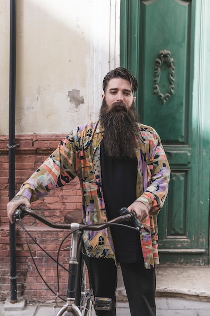 Foto gratuita retrato de un hombre de barba con su bicicleta mirando a cámara