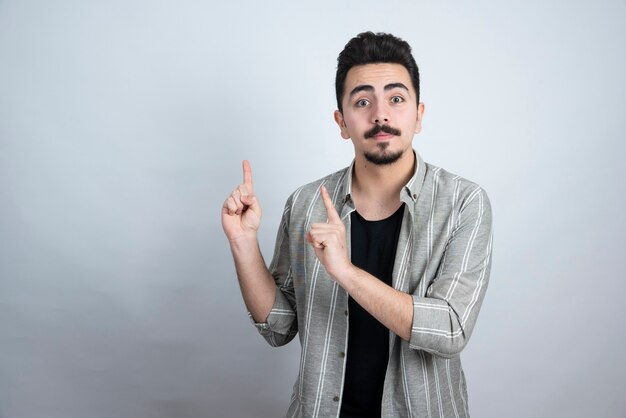 Retrato de hombre barbudo apuntando a algún lugar sobre la pared blanca.