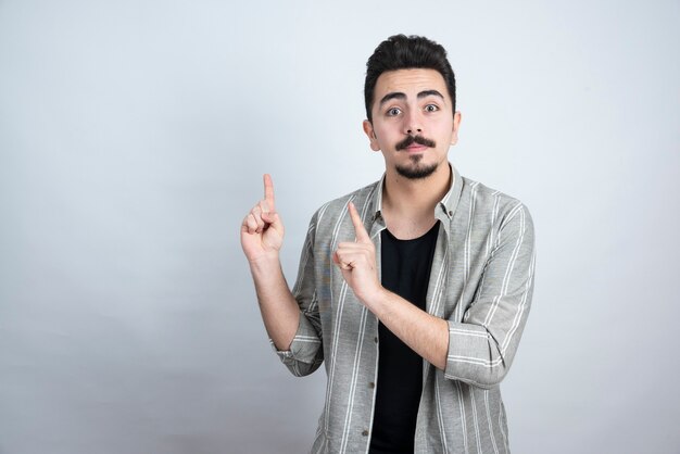 Retrato de hombre barbudo apuntando a algún lugar sobre la pared blanca.