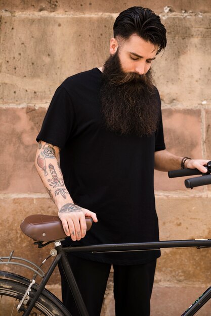 Retrato de un hombre barbudo con la bicicleta de pie delante de la pared