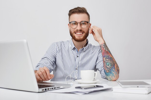 Retrato de hombre barbudo complacido encantador con peinado de moda escucha la pista de audio con auriculares