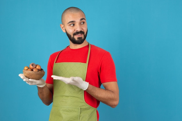 Retrato de un hombre barbudo en delantal sosteniendo un cuenco de madera de frutos secos.