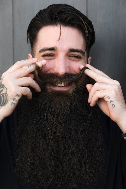 Retrato del hombre barbudo elegante joven que gira el bigote y que mira la cámara