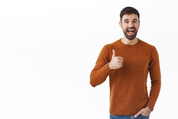 Retrato de un hombre barbudo entusiasta y apuesto como su idea, muestra el pulgar hacia arriba y sonríe complacido satisfecho con un buen plan, elogie el gran trabajo, dé su aprobación como algo de fondo blanco.