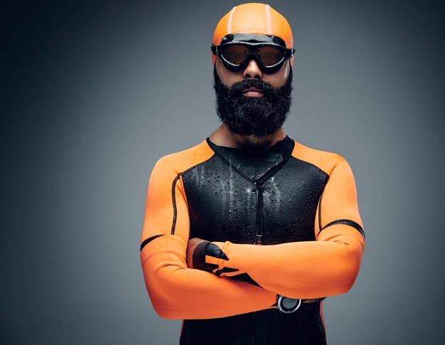 Retrato de hombre barbudo con máscara de buceo y traje de buceo de neopreno naranja aislado en fondo gris.