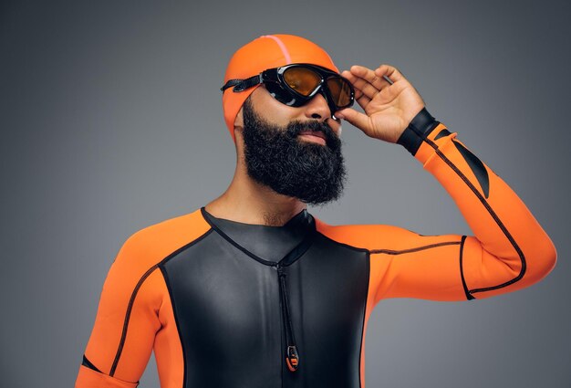 Retrato de hombre barbudo con máscara de buceo y traje de buceo de neopreno naranja aislado en fondo gris.