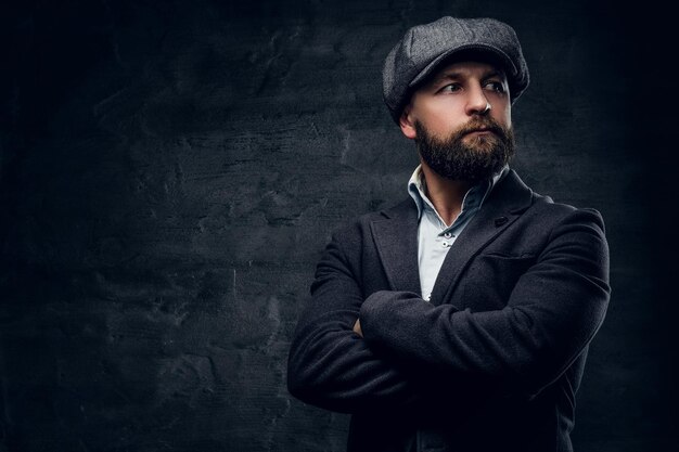 Retrato de un hombre barbudo de mediana edad con los brazos cruzados sobre el pecho, vestido con un traje de lana y una gorra de tweed.