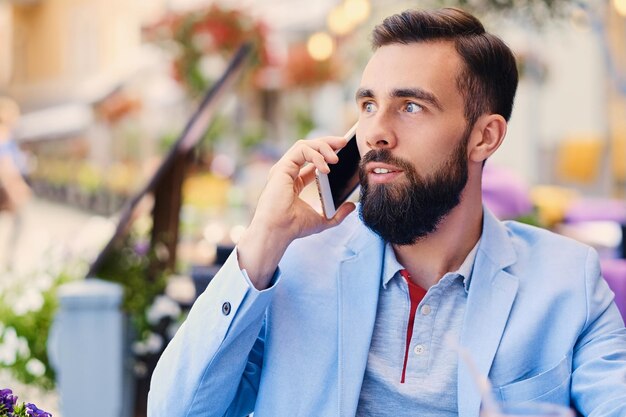 Retrato de hombre barbudo de moda en una chaqueta azul habla por teléfono inteligente.