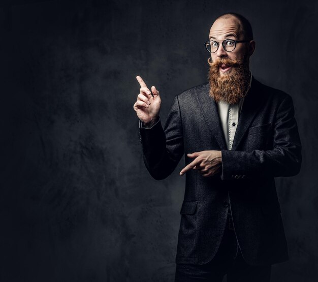 Retrato de hombre barbudo pelirrojo con anteojos vestido con un elegante traje de lana sobre fondo gris.