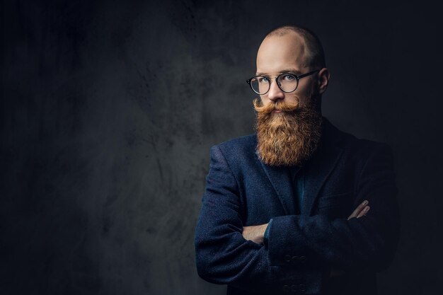 Retrato de hombre barbudo pelirrojo con anteojos vestido con un elegante traje de lana sobre fondo gris.