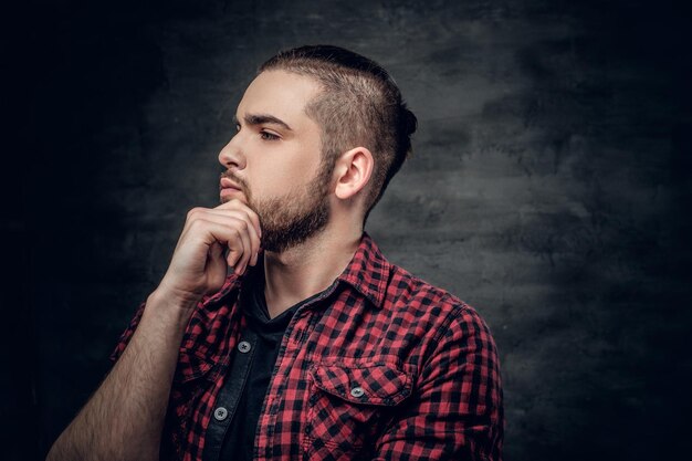 Retrato de hombre barbudo pensativo vestido con una camisa de lana roja sobre fondo gris.