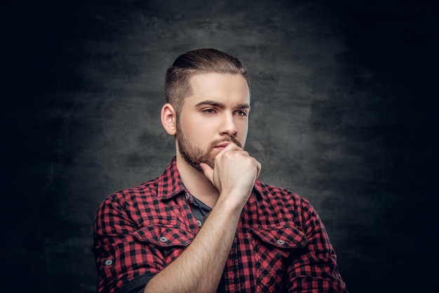 Retrato de hombre barbudo pensativo vestido con una camisa de lana roja sobre fondo gris.