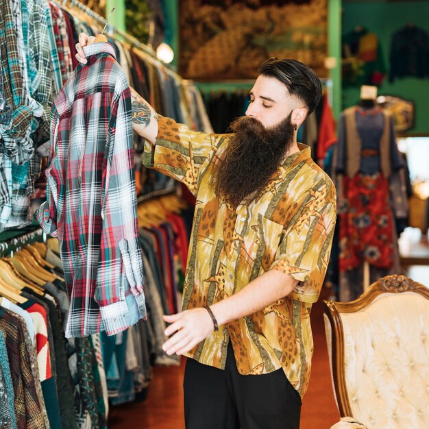 Retrato de un hombre barbudo que mira la camisa de tela escocesa en tienda de ropa