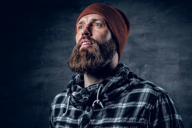 Retrato de hombre barbudo con sombrero y camisa polar sobre fondo gris oscuro.