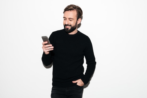 Retrato de un hombre barbudo sonriente enviando mensajes de texto por teléfono móvil