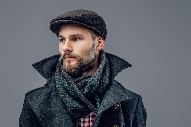 Retrato de hombre barbudo vestido con una chaqueta gris y un sombrero aislado sobre fondo gris.