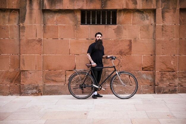 Retrato de un hombre con la bicicleta de pie delante de la pared roja