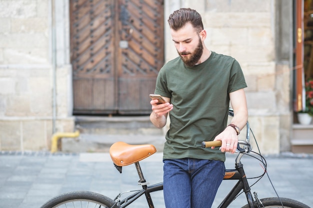 Retrato de un hombre con bicicleta de pie en el teléfono móvil