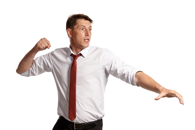 Retrato de un hombre brunet atlético con ojos marrones, vestido con una camisa blanca y una corbata roja. Él va a golpear a alguien mientras posa en un estudio aislado sobre un fondo blanco. Concepto de gesticulación