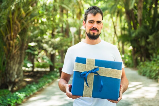 Retrato de un hombre con caja de regalo azul en el parque