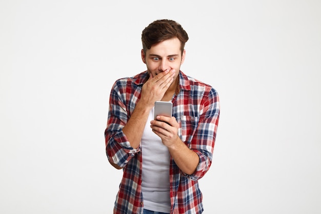 Retrato de un hombre casual sorprendido mirando el teléfono móvil