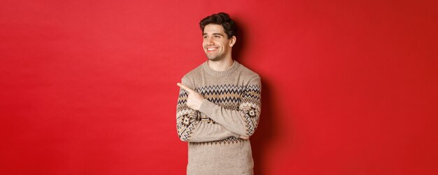 Retrato de hombre caucásico atractivo celebrando año nuevo vacaciones de invierno señalando con el dedo y mirando ...