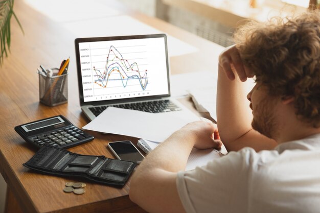 Retrato de hombre caucásico desesperado y desesperado viendo gráficos financieros y económicos durante la cuarentena de coronavirus, problemas