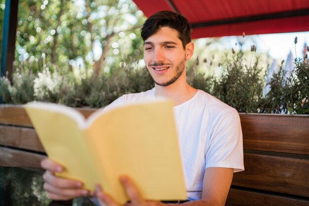 Retrato de hombre caucásico disfrutando de tiempo libre y leyendo un libro mientras está sentado al aire libre en la cafetería. Concepto de estilo de vida.