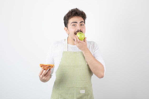 Retrato de hombre cocinero comiendo manzana en lugar de pizza en blanco